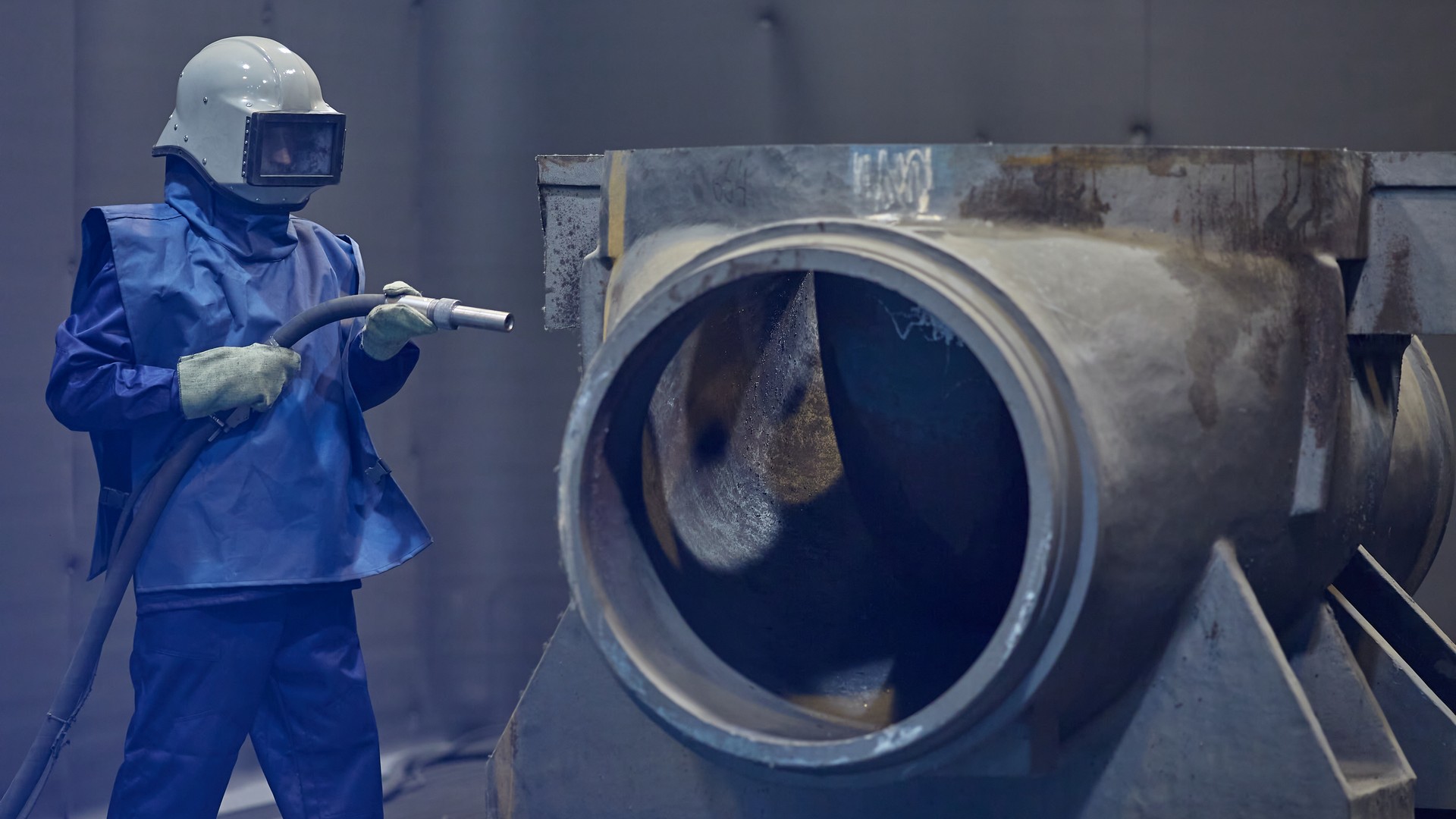 worker processes workpiece with sandblasting tool in factory, selective focus